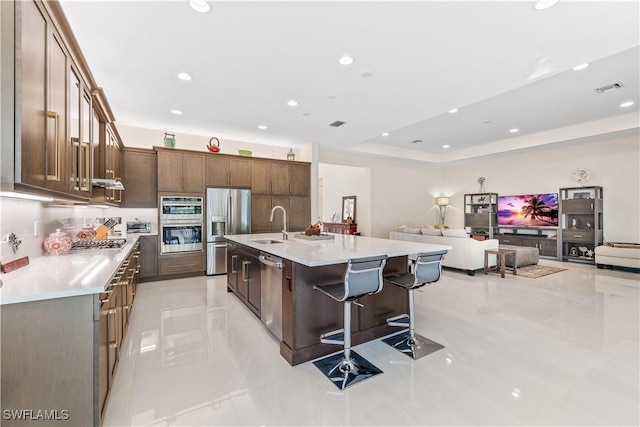 kitchen with an island with sink, a breakfast bar area, appliances with stainless steel finishes, open floor plan, and light countertops