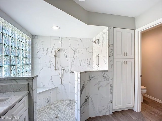 bathroom with toilet, a marble finish shower, and wood finished floors