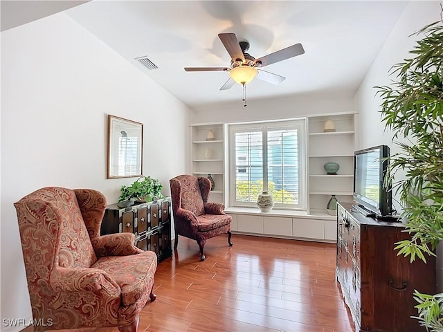 living area featuring a ceiling fan, visible vents, vaulted ceiling, and wood finished floors