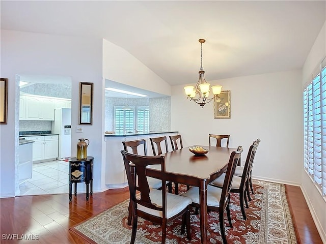 dining area featuring baseboards, vaulted ceiling, light wood finished floors, and an inviting chandelier