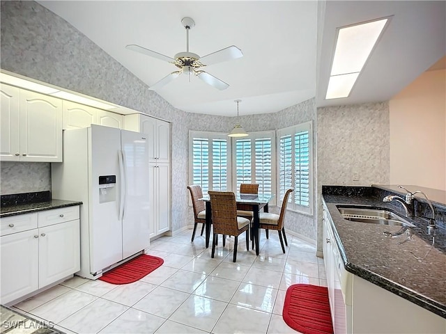 kitchen featuring ceiling fan, a sink, white fridge with ice dispenser, dark stone countertops, and wallpapered walls