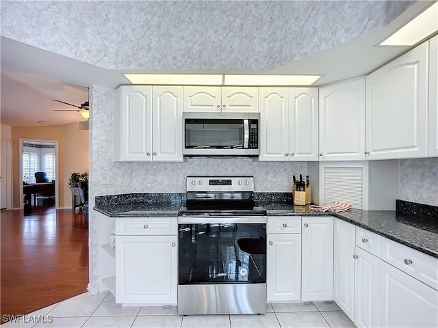 kitchen with light tile patterned flooring, a ceiling fan, white cabinets, appliances with stainless steel finishes, and dark stone counters