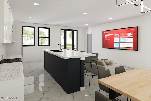 kitchen featuring stainless steel gas stovetop, white cabinetry, a kitchen bar, a notable chandelier, and a kitchen island with sink