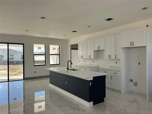 kitchen with light stone countertops, white cabinetry, sink, and a kitchen island with sink