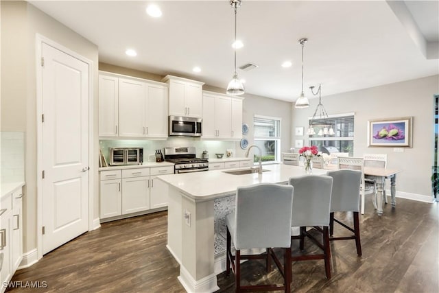 kitchen with pendant lighting, appliances with stainless steel finishes, sink, and a center island with sink