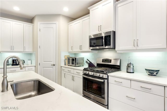 kitchen with sink, appliances with stainless steel finishes, tasteful backsplash, light stone counters, and white cabinets