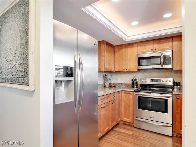 kitchen with stainless steel appliances, tasteful backsplash, a raised ceiling, light hardwood / wood-style flooring, and light stone counters