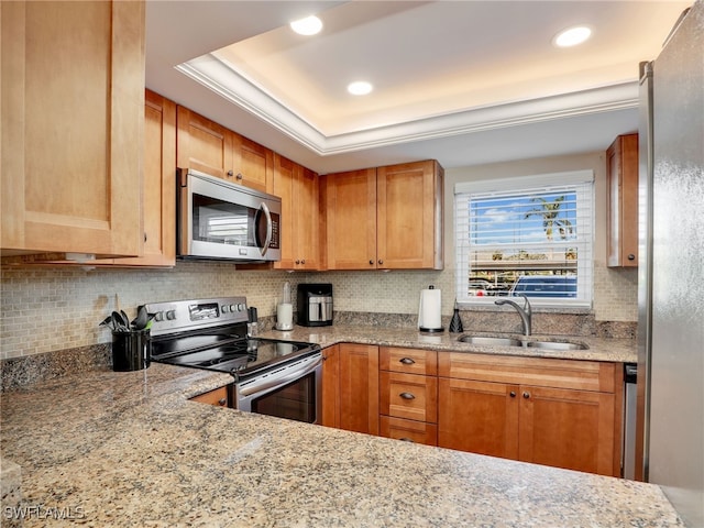 kitchen with appliances with stainless steel finishes, backsplash, a tray ceiling, light stone countertops, and sink