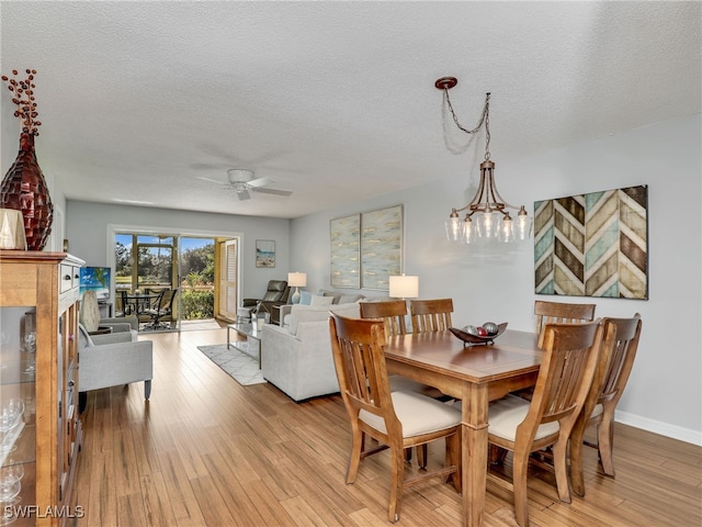 dining area with ceiling fan with notable chandelier, a textured ceiling, and light hardwood / wood-style flooring