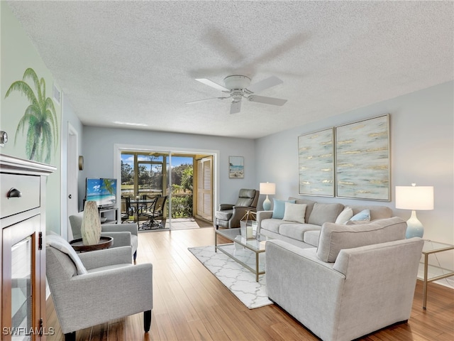 living room featuring light wood-type flooring, ceiling fan, and a textured ceiling