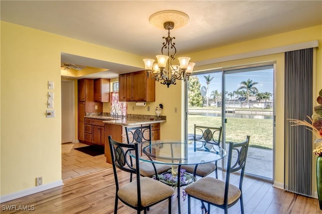 dining room featuring a notable chandelier, light hardwood / wood-style flooring, sink, and a water view