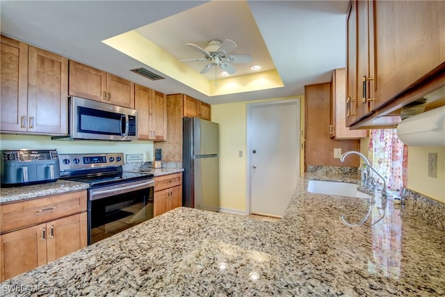 kitchen with sink, appliances with stainless steel finishes, light stone counters, kitchen peninsula, and a raised ceiling