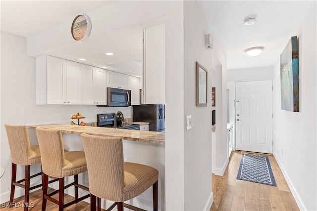 kitchen featuring white cabinets, a kitchen breakfast bar, appliances with stainless steel finishes, and light hardwood / wood-style flooring