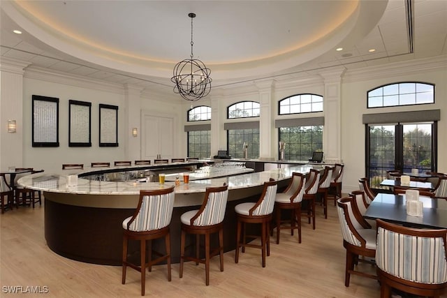 bar with decorative light fixtures, light hardwood / wood-style floors, a raised ceiling, and dark stone counters