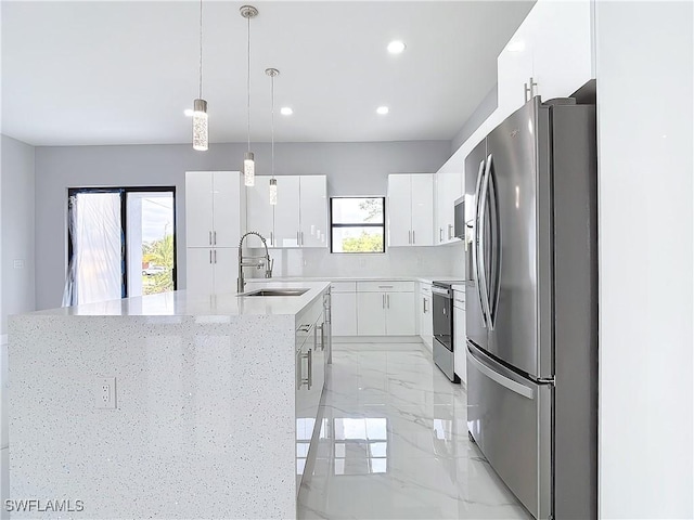 kitchen featuring pendant lighting, sink, appliances with stainless steel finishes, white cabinetry, and a kitchen island with sink