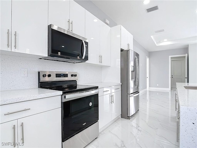 kitchen with stainless steel appliances, white cabinetry, light stone countertops, and tasteful backsplash