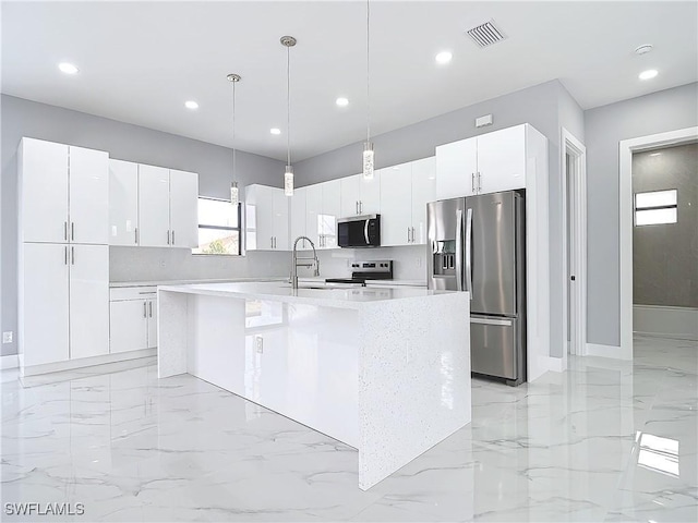 kitchen with sink, appliances with stainless steel finishes, white cabinetry, a center island with sink, and decorative light fixtures