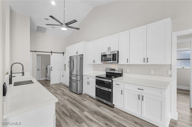 kitchen with white cabinets, appliances with stainless steel finishes, washing machine and dryer, sink, and a barn door