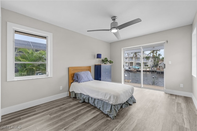 bedroom with ceiling fan, hardwood / wood-style floors, access to outside, and a water view