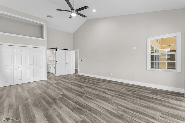 unfurnished bedroom with ceiling fan, a barn door, light wood-type flooring, high vaulted ceiling, and a closet