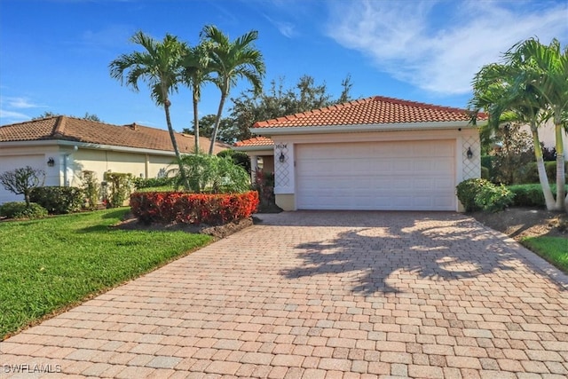 view of front of home featuring a garage, a tile roof, decorative driveway, a front lawn, and stucco siding