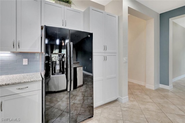 kitchen with black refrigerator with ice dispenser, white cabinetry, decorative backsplash, light stone counters, and light tile patterned floors