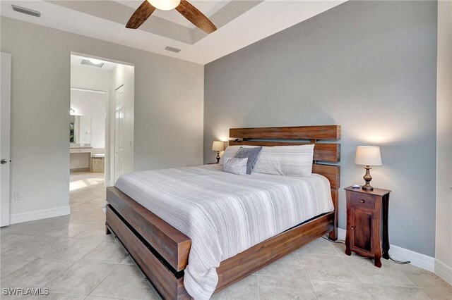 bedroom featuring ceiling fan, light tile patterned flooring, connected bathroom, and a tray ceiling