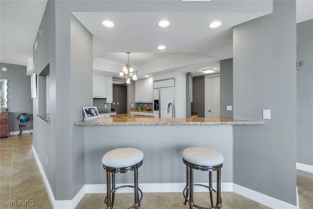 kitchen featuring light stone countertops, white cabinets, a kitchen bar, hanging light fixtures, and kitchen peninsula