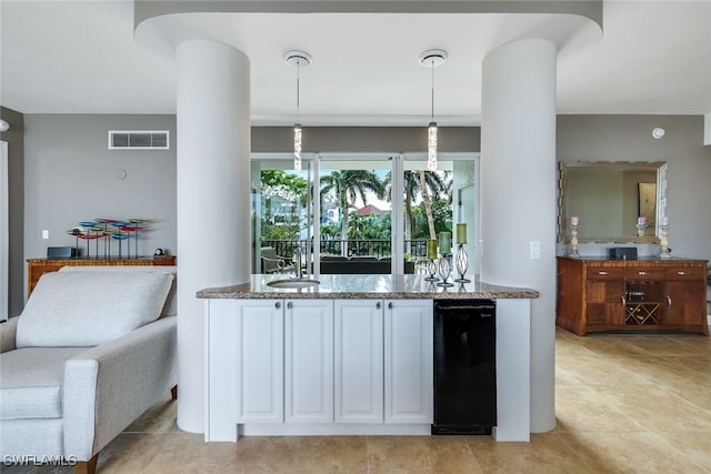 kitchen featuring white cabinets, sink, stone countertops, hanging light fixtures, and light tile patterned floors