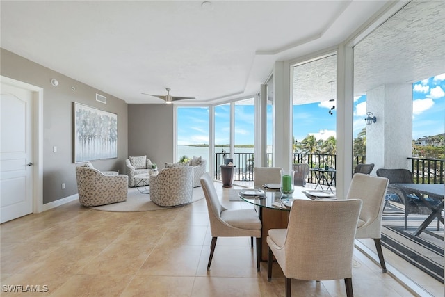 dining room with ceiling fan, a wall of windows, and a water view