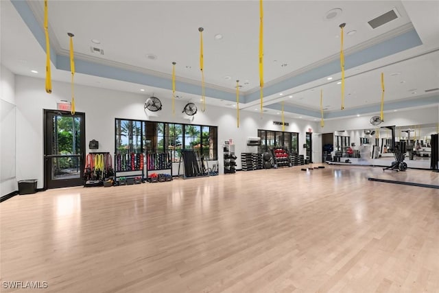 gym featuring ornamental molding, light hardwood / wood-style floors, and a tray ceiling