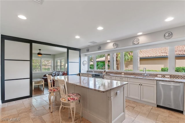 kitchen with sink, light stone countertops, stainless steel dishwasher, white cabinets, and a center island