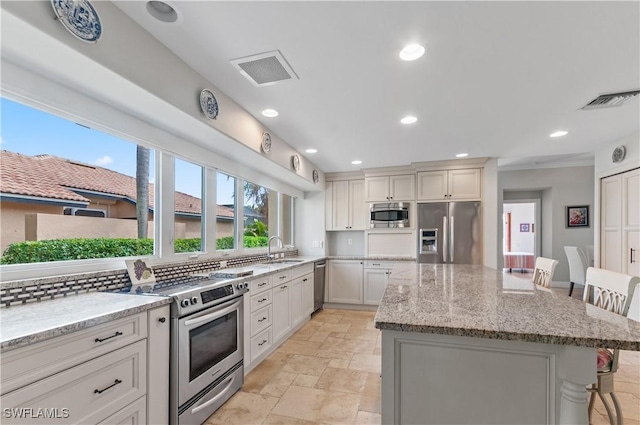 kitchen featuring tasteful backsplash, a center island, a kitchen bar, light stone countertops, and stainless steel appliances