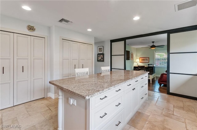 kitchen with light stone countertops, white cabinets, a kitchen island, a kitchen bar, and ceiling fan