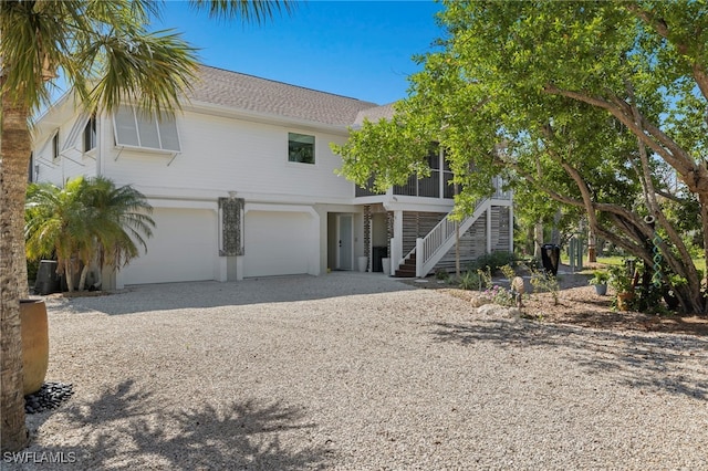 raised beach house featuring driveway, a sunroom, a garage, and stairs