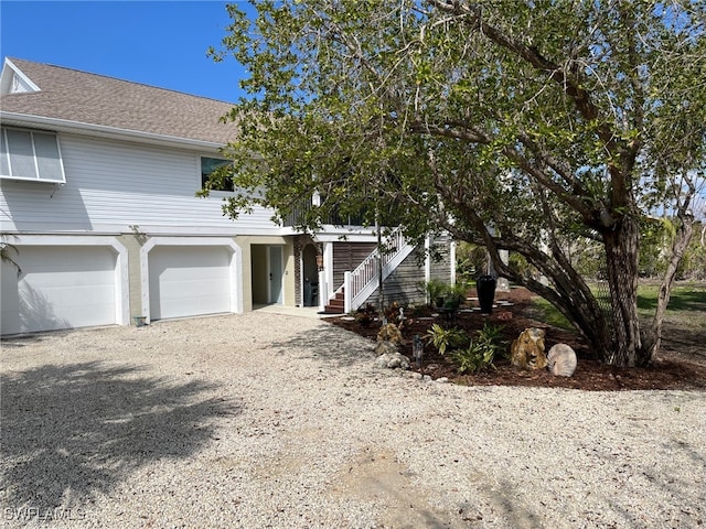 view of front of home with driveway, a shingled roof, a garage, and stairway