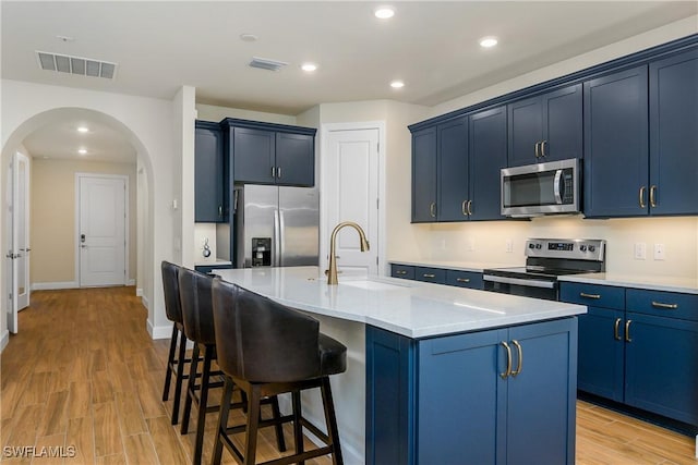 kitchen featuring sink, appliances with stainless steel finishes, an island with sink, and blue cabinets