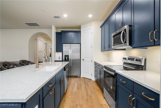 kitchen featuring a center island with sink, sink, light hardwood / wood-style flooring, appliances with stainless steel finishes, and blue cabinetry