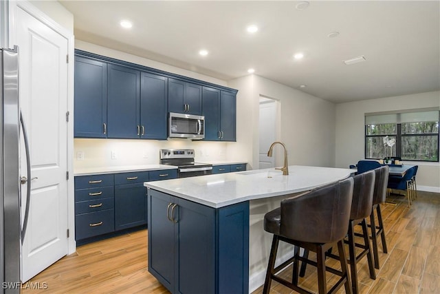 kitchen featuring an island with sink, blue cabinets, sink, and stainless steel appliances