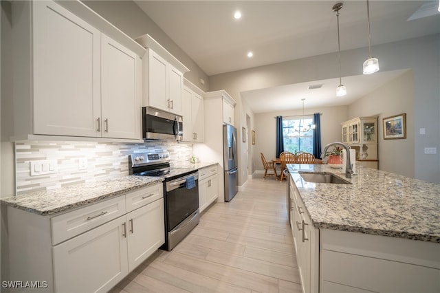 kitchen with white cabinets, decorative light fixtures, stainless steel appliances, an island with sink, and sink