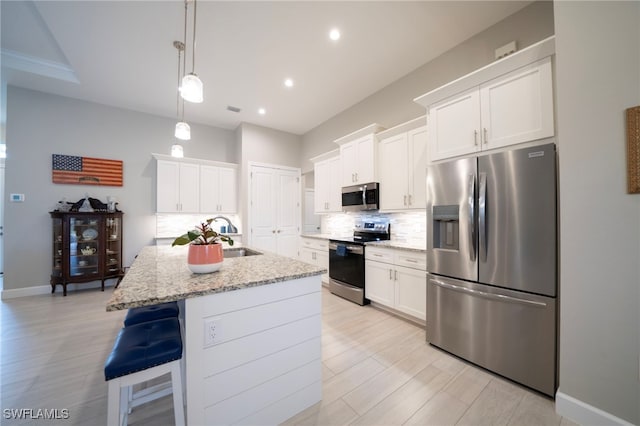 kitchen featuring white cabinets, light stone countertops, an island with sink, and stainless steel appliances