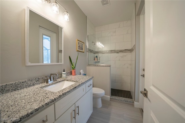 bathroom featuring tiled shower, vanity, and toilet