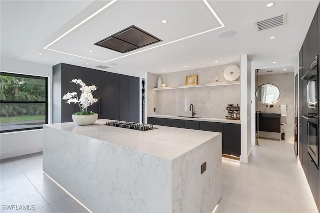 kitchen featuring sink, light tile patterned floors, a kitchen island, light stone countertops, and black gas stovetop