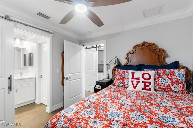 bedroom featuring ensuite bath, light wood-type flooring, ceiling fan, crown molding, and a barn door