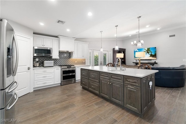 kitchen with an island with sink, stainless steel appliances, hanging light fixtures, white cabinets, and sink