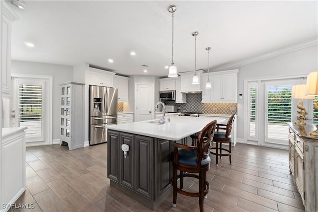 kitchen with a center island with sink, appliances with stainless steel finishes, backsplash, hanging light fixtures, and white cabinets