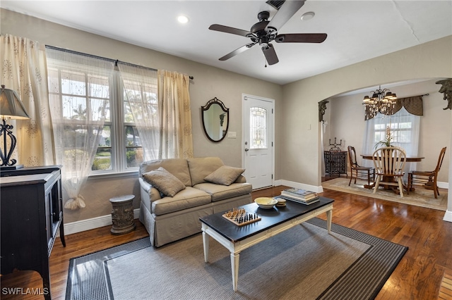 living room with ceiling fan with notable chandelier, dark wood-type flooring, and a wealth of natural light