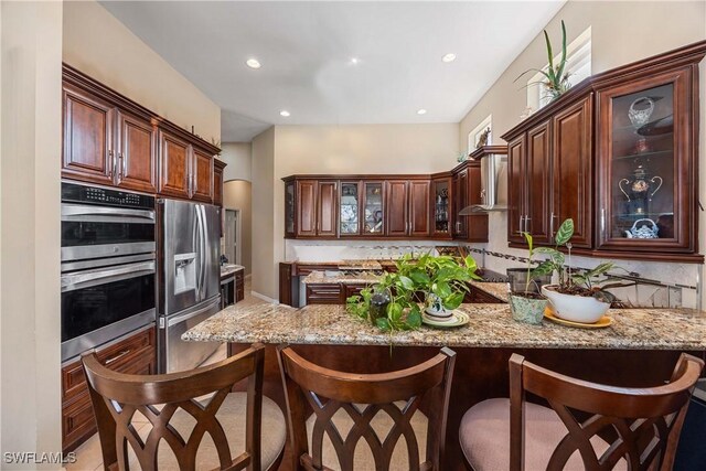 kitchen with light stone countertops, appliances with stainless steel finishes, a kitchen breakfast bar, and kitchen peninsula