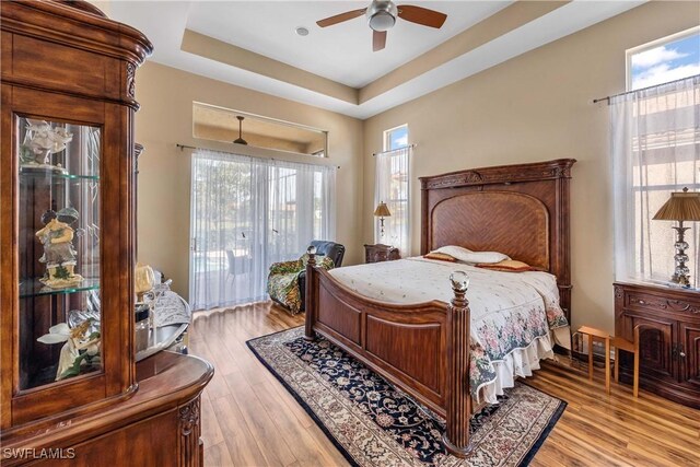 bedroom featuring a raised ceiling, access to outside, ceiling fan, and light hardwood / wood-style flooring