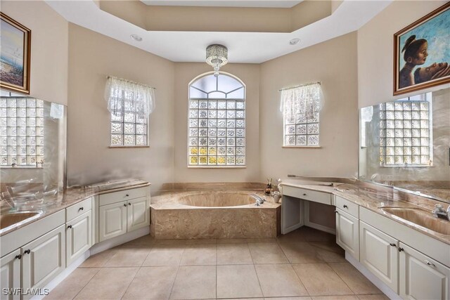 bathroom featuring tile patterned flooring, vanity, tiled tub, and a tray ceiling